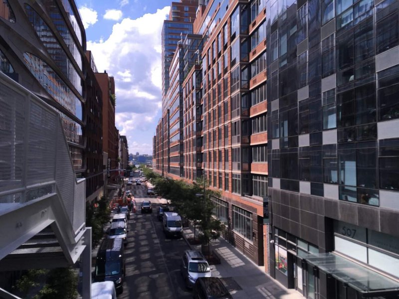 Street in the middle of the city with parked cars and buildings on both sides, opening to the sea, cloud, blue sky in the distance.jpg